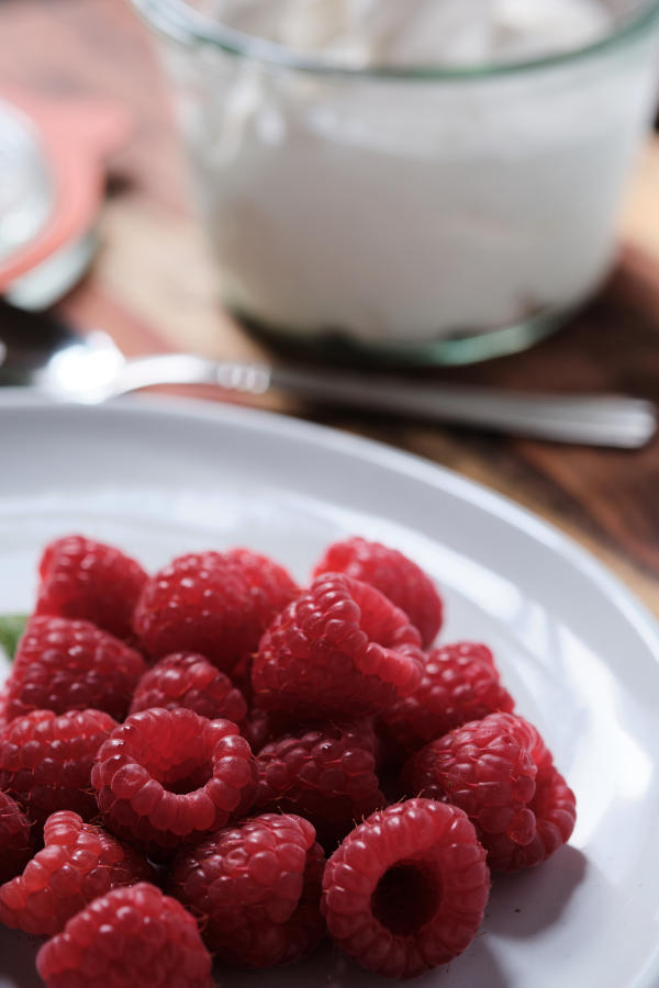 Raspberries on a plate with a spoon and jar in the background.